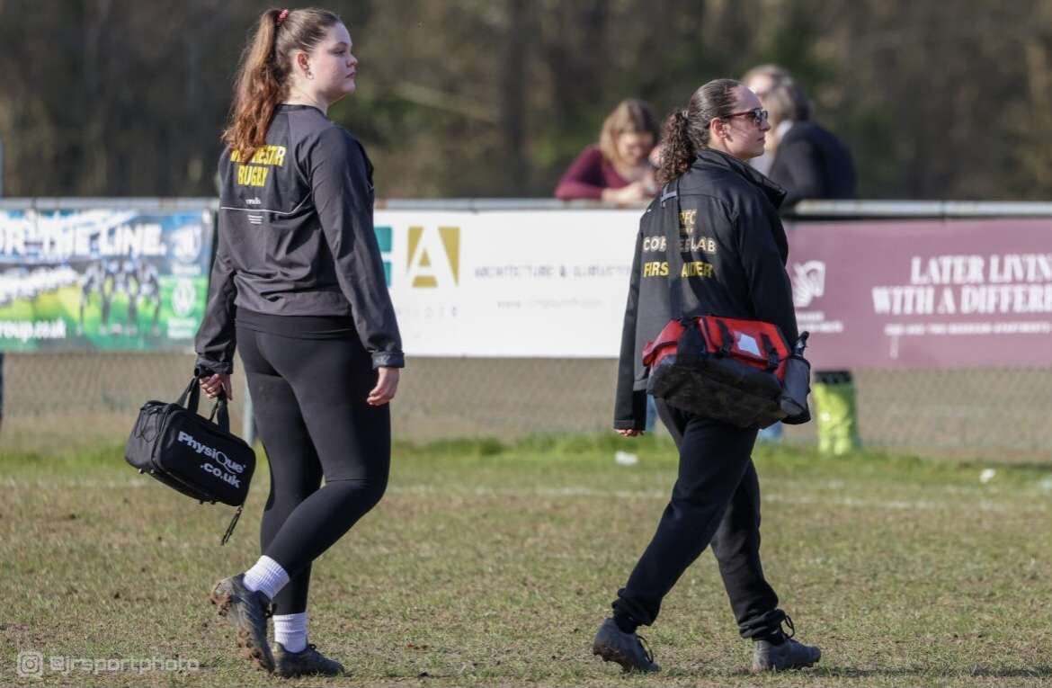 Two first aiders walking along the touchline with kit bags at a rugby match